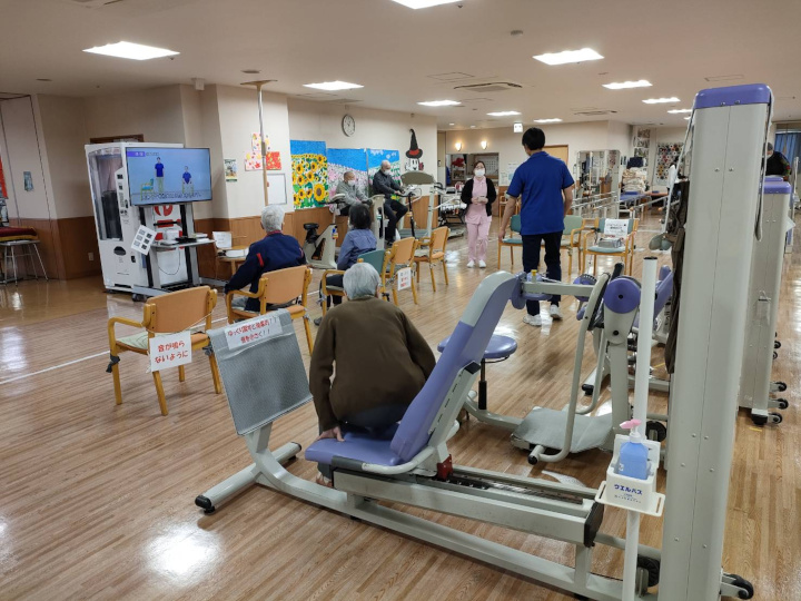 通所リハビリの利用者と機能訓練機器、スタッフがいる室内