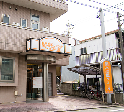 公式医院紹介ページ掲載。藤本歯科クリニックの名称サインと入口が分かる外観。