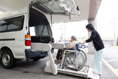 車椅子利用者の送迎車乗車を職員が支える場面