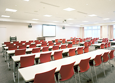 公式の心理教育・家族相談会ページに掲載された机と椅子のある講堂