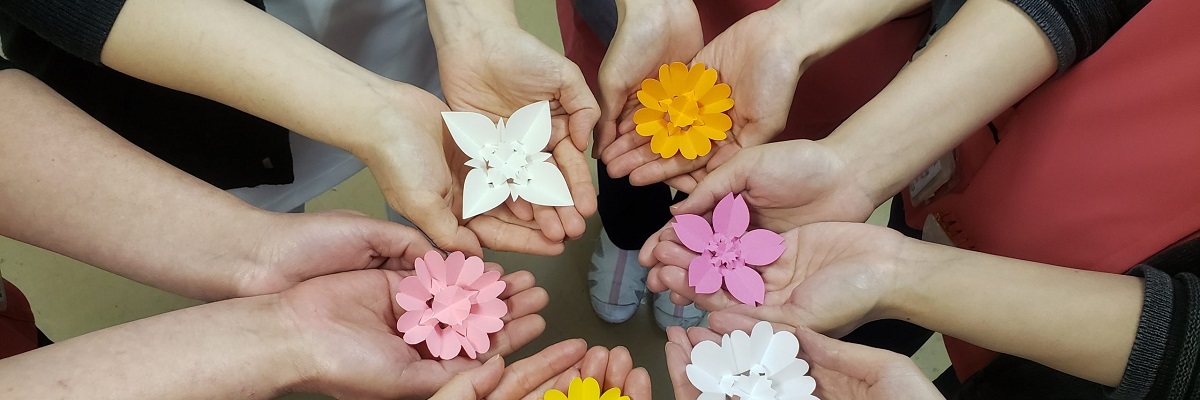 職員が手のひらに色紙の花を持つ地域活動の写真