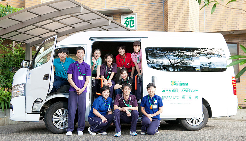 公式リハビリテーション部紹介に掲載された法人名表示の訪問車両とスタッフ