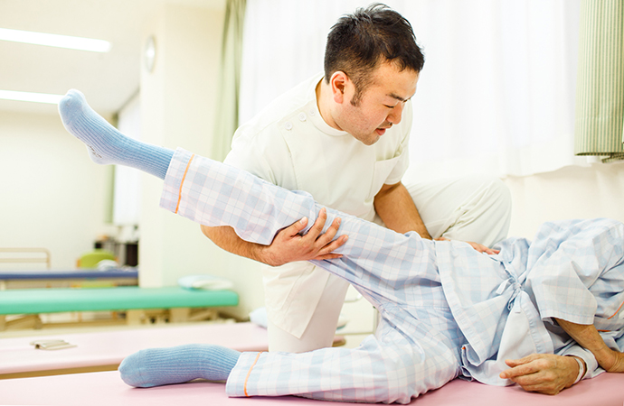 療法士がベッド上で利用者の下肢の動きを支援する様子