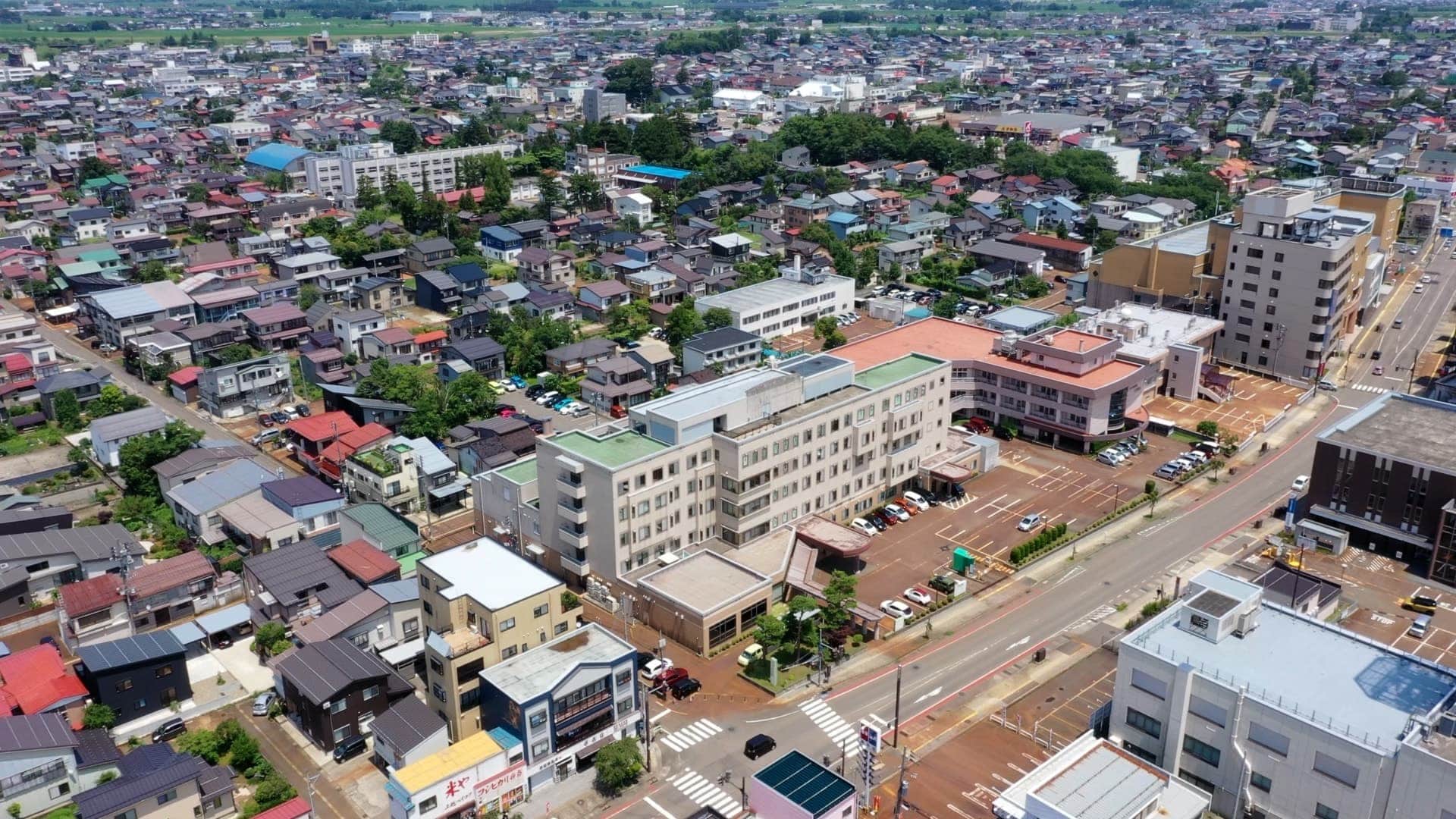 公式トップのキービジュアル。知命堂病院の建物と周辺の上越市街を写す空撮