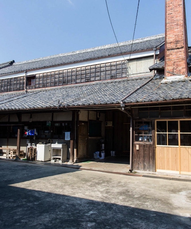 公式ギャラリーの、元坂酒造株式会社の看板前に立つ蔵人