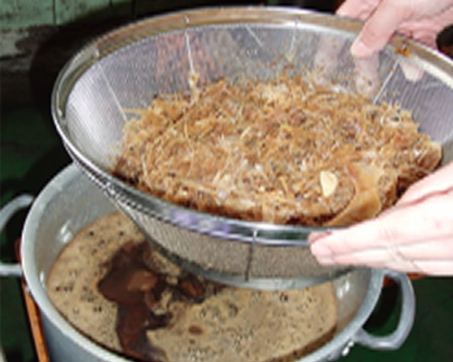 熟成した魚醤の原料をざるで搾る手元
