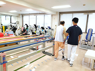 公式リハビリテーション科ページに掲載される、スタッフが歩行訓練を支えるリハビリ室の様子