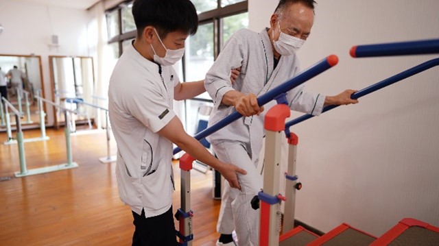 リハビリ室でスタッフが患者の歩行訓練を支える様子