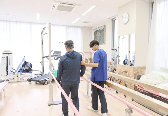 スタッフが平行棒での歩行練習を支援する様子