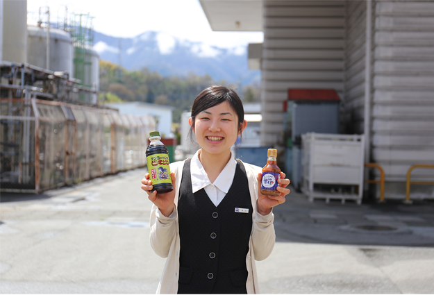 公式社員紹介に掲載される工場前で商品を手にするスタッフ