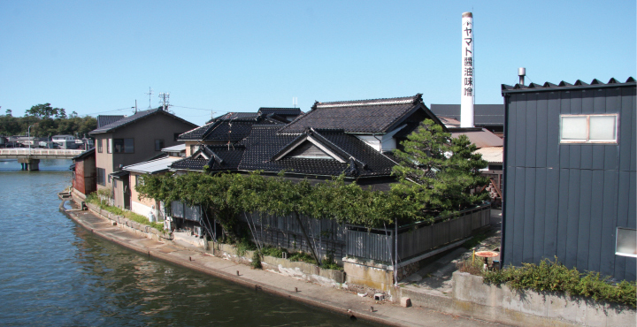 公式会社概要に掲載された水辺に建つヤマト醤油味噌の蔵と煙突