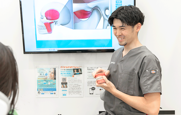 公式の初診案内ページに掲載された、模型を使って説明する歯科医師